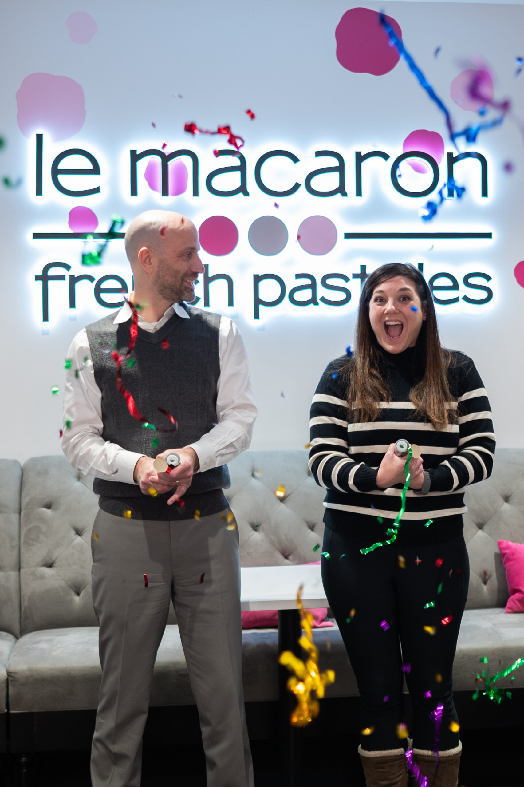 Le Macaron Fishers is celebrating its first birthday. Owners Aaron and Christi Parker have confetti to celebrate in front of the Le Macaron French Pastries sign in their cafe.